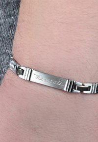 Bracciale in acciaio inossidabile argento con chiusura a cerniera e una placca incisa "Maserati"; i link testurizzati creano un aspetto moderno.