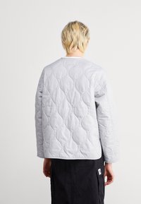 Pikowana szara kurtka z okrągłym dekoltem i długimi rękawami. Charakteryzuje się falistym wzorem i miękką fakturą, zestawiona z ciemną spódnicą.