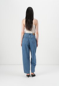 Visoke, široke kavbojke v modri barvi z svetlim pranjem in subtilnim zbledeljem. Imajo zadnje žepke in svetlosrni usnjeni pečat na pasu.