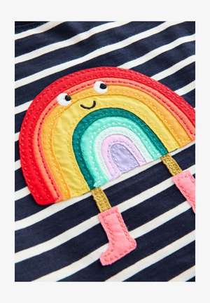 Csíkos ing, amely piros, narancssárga, sárga, zöld, türkiz és lila színű hímzett szivárvány mintával rendelkezik, rózsaszín csizmával és mosolygó arccal.