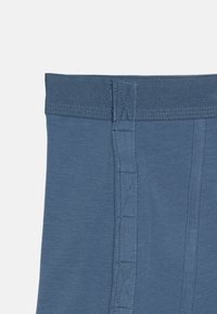 Tela de algodón azul con una textura suave, que presenta una cintura plana y un sutil detalle de costura a lo largo de la costura lateral.