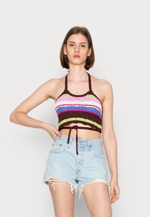 Top de crochê com decote halter, apresentando listras horizontais multicoloridas em rosa, verde, azul e castanho, combinado com calções de jeans claros e desgastados.