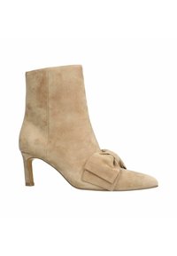 Beige suède enkellaars met een puntige neus, een strikaccent aan de voorkant en een slanke, ongeveer 7,5 cm hoge hak. Soepele textuur.