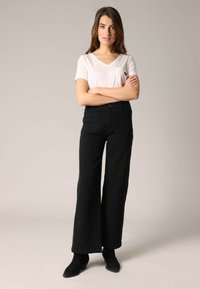 Zwarte wijde broek gemaakt van textuurstof, gecombineerd met een witte V-hals t-shirt met een kleine pocket, gedragen met zwarte enkellaarsjes.