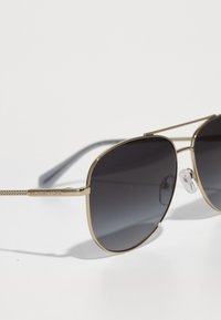 Guld metal aviator solbriller med gradient mørke linser. Funktioner inkluderer en dobbelt bro og teksturerede stænger med indgraveret branding.
