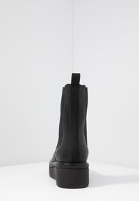 Botín negro hasta el tobillo con cuero liso y paneles laterales elásticos. Cuenta con una tira en el talón y una suela de goma gruesa.