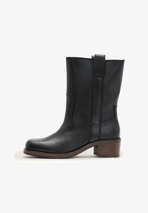 Musta nahkainen puolivartinen saapas pyöreällä kärjellä, vetokahvalla ja ruskealla paksulla korolla valkoisella taustalla.