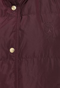 Bordo jastučić s zlatnim dugmadima, s izvezenim logotipom. Glatka tekstura i prilagođeni dizajn bez vidljivih džepova.