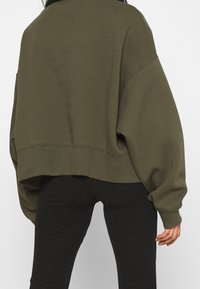 Olive green cropped sweatshirt with drop shoulders, ribbed cuffs and hem, paired with black ribbed high-waisted pants. Smooth texture.