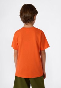 Camiseta de algodón naranja con mangas cortas, escote redondo y una textura suave. Vista desde la parte posterior, combinada con pantalones cortos verdes.