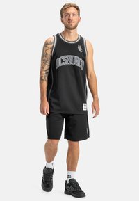 Čierny basketbalový dres z jemnej sieťoviny s bielymi akcentmi a logom, doplnený čiernymi šortkami. Nosené s čiernymi teniskami a bielymi ponožkami.