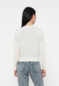Pull léger de couleur crème avec manches longues, bords côtelés et ourlet ; présente une texture légèrement transparente et une coupe décontractée.