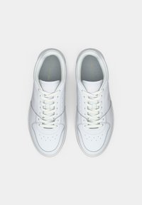 White leather sneakers with round toe, perforated detailing, flat laces, and a light gray inner lining. Features a logo on the tongue.