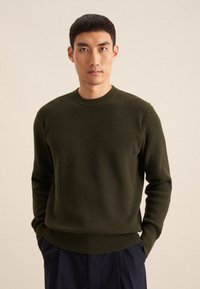 Pull en tricot côtelé vert olive avec un col rond, des manches longues et une coupe décontractée, présentant un tissu texturé et un ourlet droit.