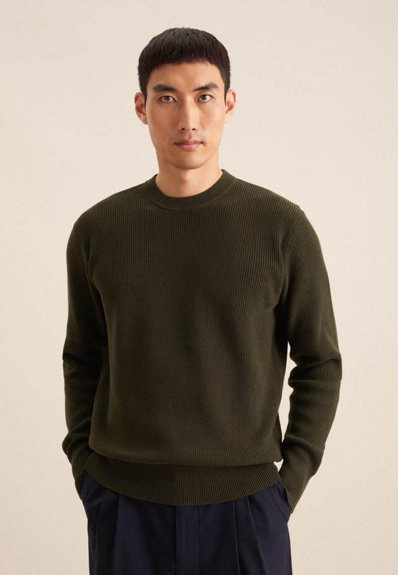 Pull en tricot côtelé vert olive avec un col rond, des manches longues et une coupe décontractée, présentant un tissu texturé et un ourlet droit.