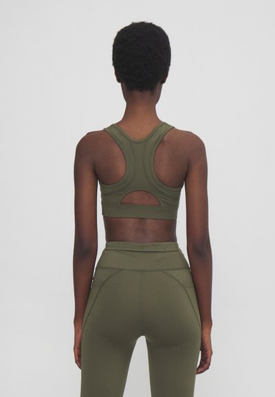 Olive green sports bra with a racerback design and cut-out detail. The material appears smooth and fitted, complementing high-waisted leggings.