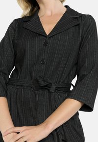 Musta-valkoinen raidoitettu mekko, jossa on kaulus, kolmanneksen pituiset hihat ja vyöllinen vyötärö. Mukana napp closure ja herringbone-kuvio.