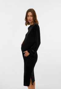 Vestido de maternidad negro en tejido suave y elástico, con mangas largas y una abertura lateral, diseñado para ajustarse cómodamente sobre una barriga redondeada.