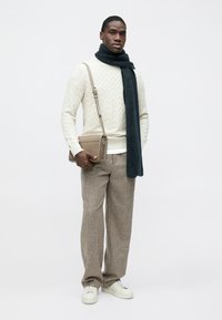 Pull clair texturé avec une écharpe noire, associé à un pantalon marron ample et des baskets blanches, avec un petit sac à bandoulière beige.