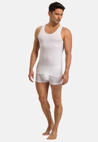 Bílý top bez rukávů vyrobený z hladké, pružné látky. Má kulatý výstřih a široké ramínka. K němu patří průhledné bílé šortky.
