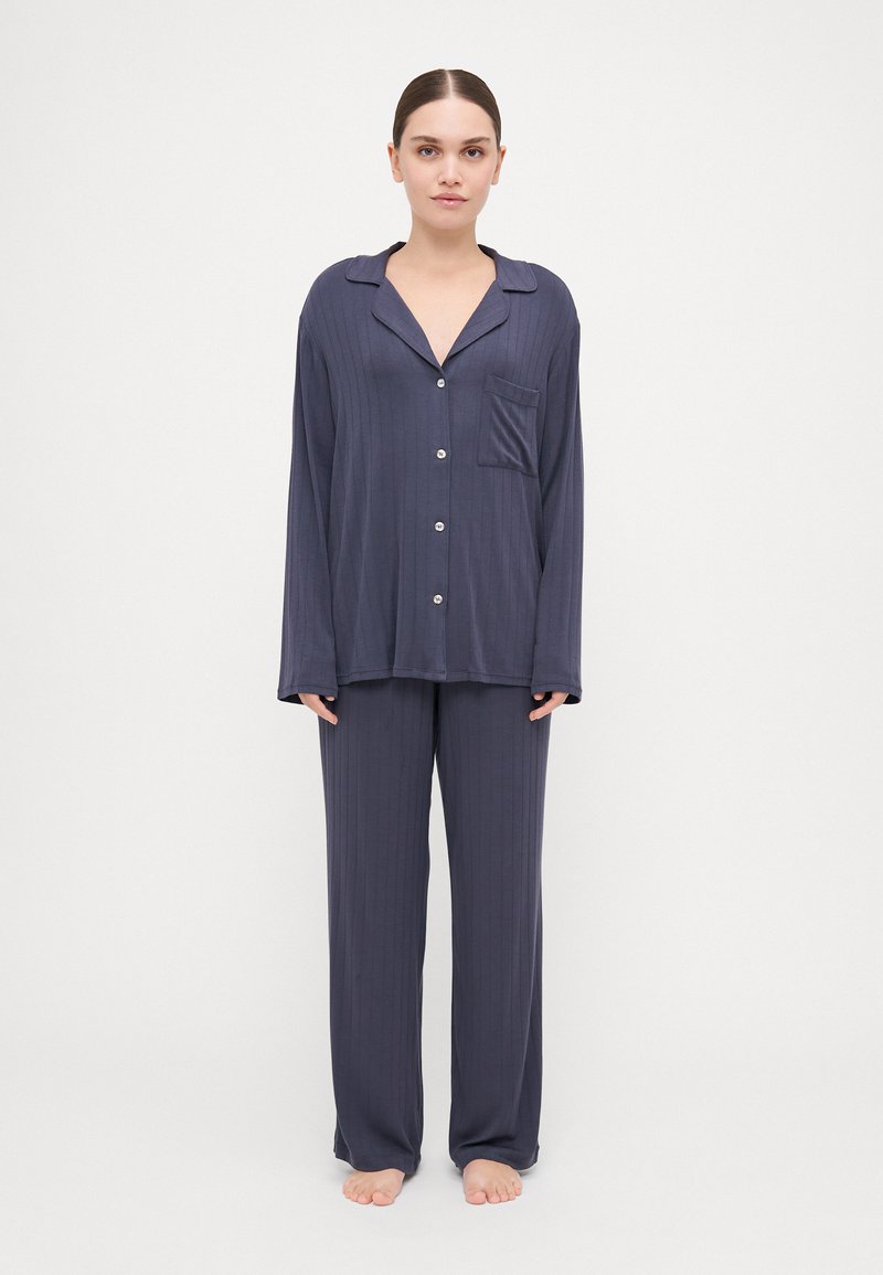 Navy blue pajama set features a button-up shirt with a collar and pocket, and loose-fitting pants, both with a subtle ribbed texture.