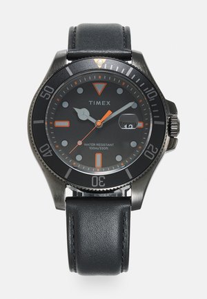 Timex watch with a black metal bezel, black dial, orange accents, and leather strap. Features include a date window and 100m water resistance.