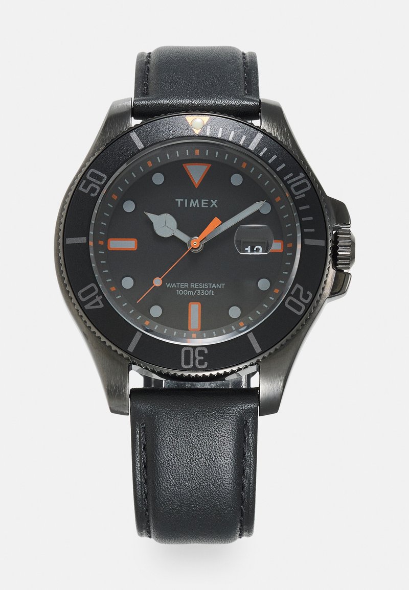 Timex pulkstenis ar melnu metāla rāmi, melnu ciparnīcu, oranžiem akcentiem un ādas siksniņu. Funkcijas ietver datuma logu un 100 m ūdens izturību.