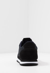 Baskets noires et bleu marine avec une tige en suède et mesh, dotées d'un talon texturé, d'une semelle intermédiaire blanche et d'un design minimaliste.