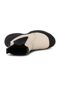 Beige och svart slip-on stövel med ett mjukt läderöverdrag, texturerad svart gummisula och en dragflik för lätt påtagning.