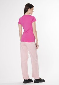 Camiseta ajustada rosa combinada con pantalones de pierna ancha de un rosa claro. Zapatos negros con suela gruesa que completan el conjunto. Diseño minimalista, textura suave.