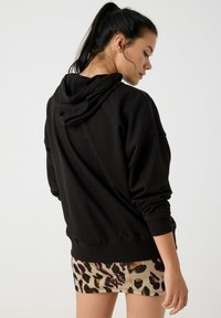 Sudadera negra de mezcla de algodón, con un corte relajado, capucha grande y puños acanalados, combinada con una falda corta de estampado de leopardo.