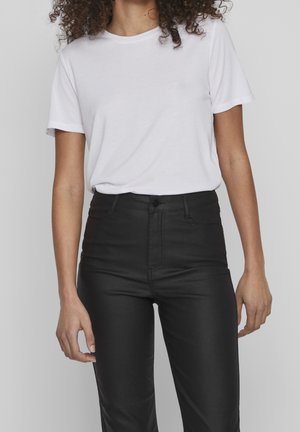 Biała koszulka z krótkim rękawem w połączeniu z czarnymi spodniami z wysokim stanem. Koszulka ma okrągły dekolt; spodnie wyposażone są w przednie kieszenie i zapięcie na guzik.