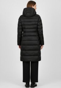 Cappotto imbottito nero con cappuccio, caratterizzato da un design trapuntato e strisce verticali. Taglio lungo fino al ginocchio con una texture liscia e accentuazioni minime.