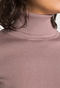 Ljusrosa ribbad polotröja med en nära sittande krage, som visar en mjuk textur och subtila sömnadsdetaljer längs halsen.