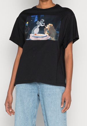 Person wearing black T-shirt with printed scene of two dogs sharing a spaghetti noodle at a candlelit table.