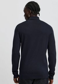 Pullover lavorato a maglia color navy con maniche lunghe e orlo a coste. Presenta un colletto classico e una texture liscia, adatto per un abbigliamento casual.