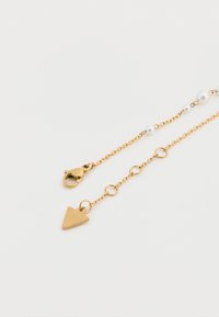 Χρυσό κολιέ αλυσίδας με μικρές λευκές πέρλες, τριγωνικό μενταγιόν και κούμπωμα με ανθοδέτη. Οι υφασμένες συνδέσεις δημιουργούν οπτικό ενδιαφέρον.