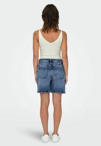 Shorts in denim blu chiaro con una finitura sbiadita, caratterizzati da una vestibilità dritta, tasche posteriori, abbinati a un top a canotta bianco a coste.