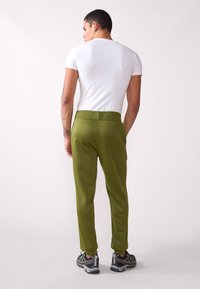 Pantalones elásticos verdes con una textura suave y una cinturilla elástica, combinados con una camiseta ajustada de manga corta blanca y zapatillas atléticas grises.