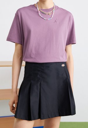 Violetti puuvillapaita lyhyillä hihoilla ja Jordan-logo, yhdistettynä mustaan laskostettuun hameeseen, jossa on logotagi ja sileä pinta.