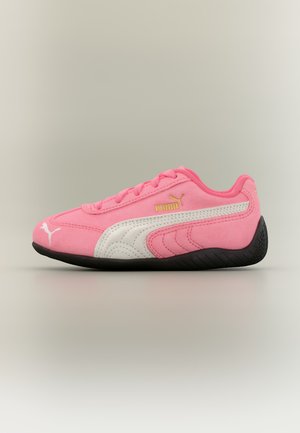 Baskets Puma roses avec bande latérale blanche, semelle noire, lacets roses et logo Puma doré sur un fond clair uni.