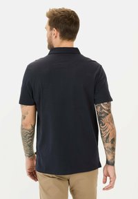 Marineblå polo-shirt med korte ærmer, en klassisk krave og en glat tekstur. Viser synlige tatoveringer på armene, ensartet design uden mønstre.