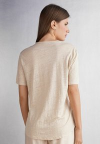 Béžové tričko s krátkým rukávem a kulatým výstřihem, vyrobené z měkké, texturované látky. Má volný střih a mírně zakřivený lem.