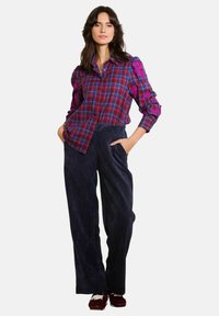 Burgundijas un jūras zila šallīte ar ziedu izšuvumiem uz piedurknēm, kombinēta ar platām jūras zila korduroja biksēm ar teksturētu audumu.