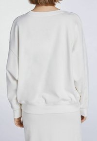 Sudadera blanca de gran tamaño con cuello redondo, hombros caídos y puños acanalados. Textura suave, diseño simple, sin patrones ni acentos.