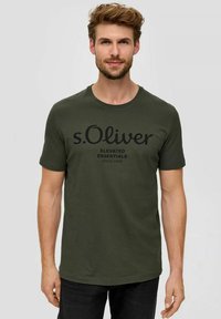 Olivgrünes T-Shirt aus Baumwolle mit Rundhalsausschnitt. Auf der Vorderseite befindet sich ein großer schwarzer Druck von "s.Oliver" und "ELEVATED ESSENTIALS".