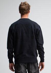 Marine sweatshirt met ronde hals, lange mouwen en textuurstof. Voorzien van grote reliëftekst op de achterkant: “BUTCHER OF BLUE CUTTERS EIGHTEEN.”