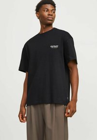 Zwarte katoen T-shirt met korte mouwen, met witte tekst "DE ZIEL ONTDEKKEN". Losse pasvorm met een gladde textuur.