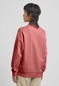 Felpa in pile di un corallo attenuato, con vestibilità rilassata, maniche lunghe e polsini a coste. Tessuto morbido e design minimalista.