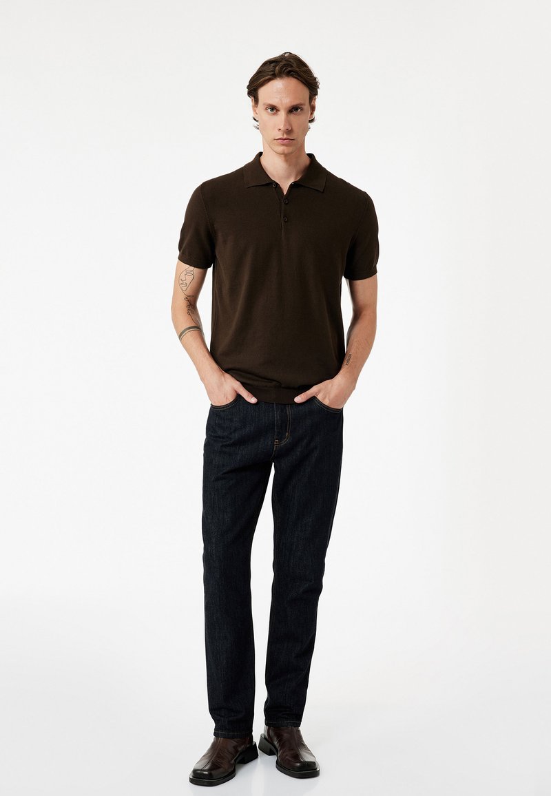 Polo de color marrón oscuro con mangas cortas y dos botones, combinado con unos pantalones vaqueros oscuros y zapatos oscuros, con un diseño ajustado.